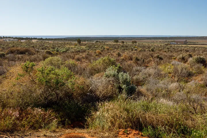 Expansive arid landscape featuring natural scrubland vegetation and distant structures under a clear sky