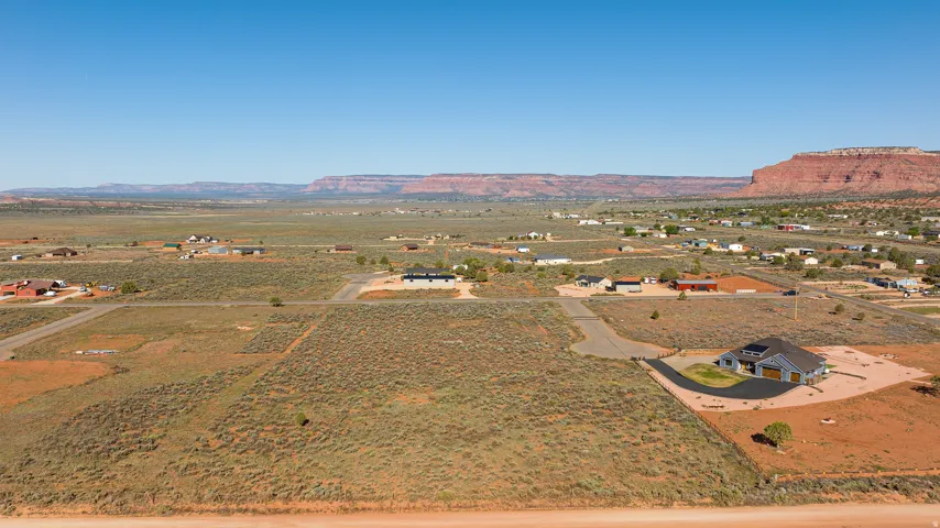 Expansive desert landscape featuring a single-family residence with a light blue exterior, a grey roof, and an attached three-car garage