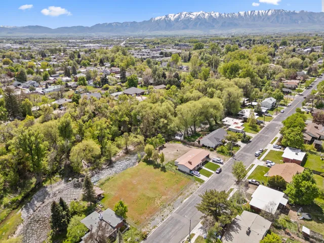 Expansive aerial capturing a suburban neighborhood with mature trees, a streetscape, and distant snow-capped mountains