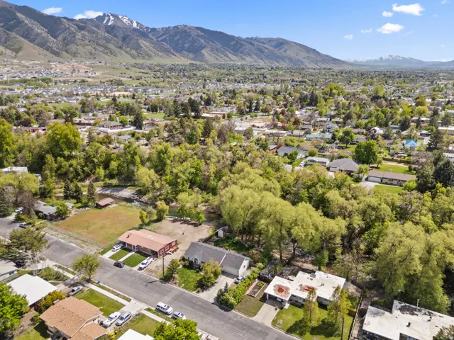 Expansive aerial showcasing a residential area with lush green trees, snow-capped mountains, and a clear blue sky