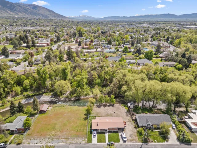 Aerial perspective showcasing a residential property with a brown roof and a paved driveway, featuring a verdant backdrop of mature trees and distant mountains