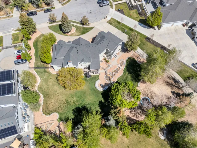 Expansive property featuring a multi-level residence with a dark shingle roof, a terraced stone hardscape, and a substantial green lawn