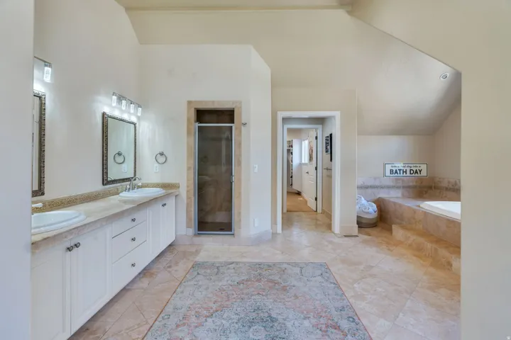 Spacious bathroom featuring twin vanity sinks, a tiled countertop, a glass-enclosed shower, a built-in soaking tub, and tile flooring