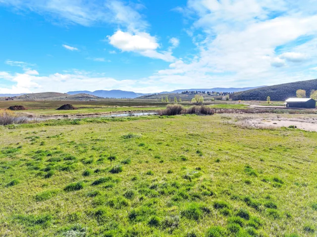 Expansive green landscape with a natural water feature, distant hills, and a barn structure