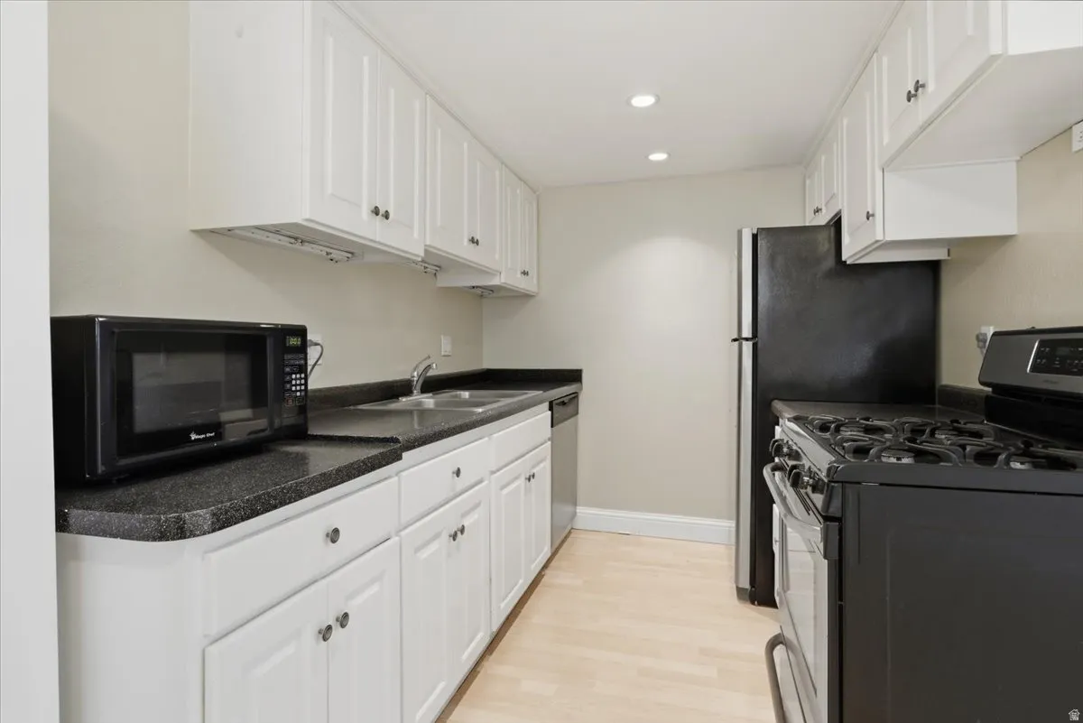 Galley kitchen featuring white cabinetry, dark countertops, a double basin sink, light wood-finish flooring, and recessed lighting