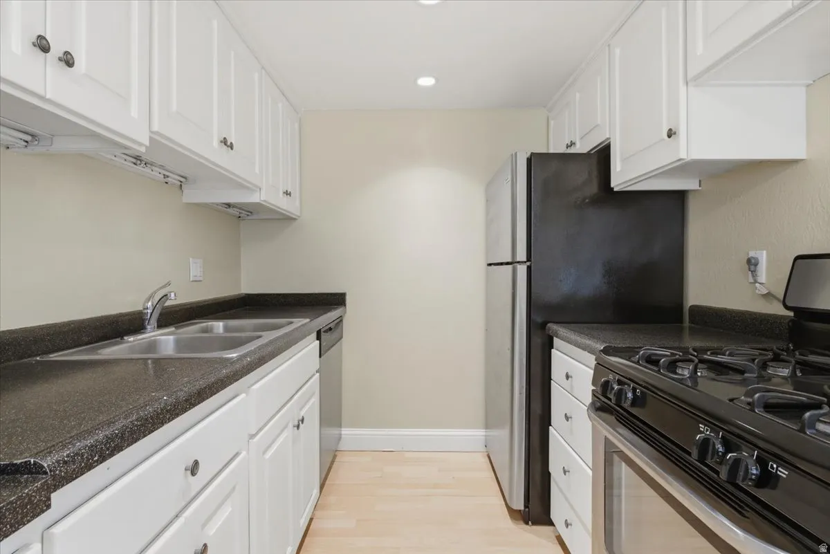 Kitchen featuring white upper and lower cabinetry, dark speckled countertops, and wood-finish flooring