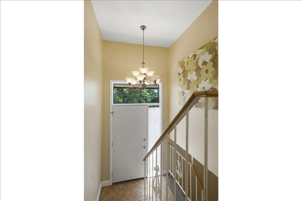 Inviting entryway featuring a white entry door with transom window, vaulted ceiling, and a multi-arm chandelier