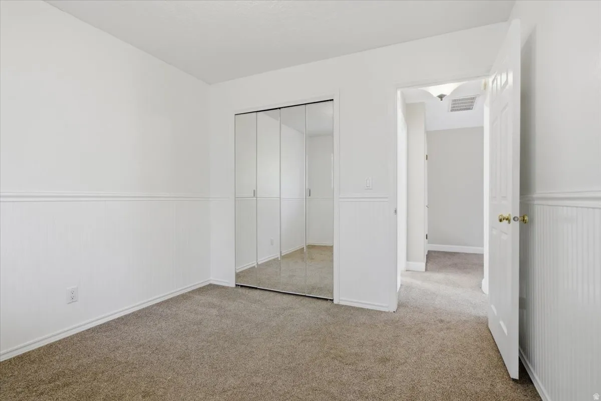 Bedroom featuring mirrored sliding closet doors, wainscoting, neutral carpeting, and white trim