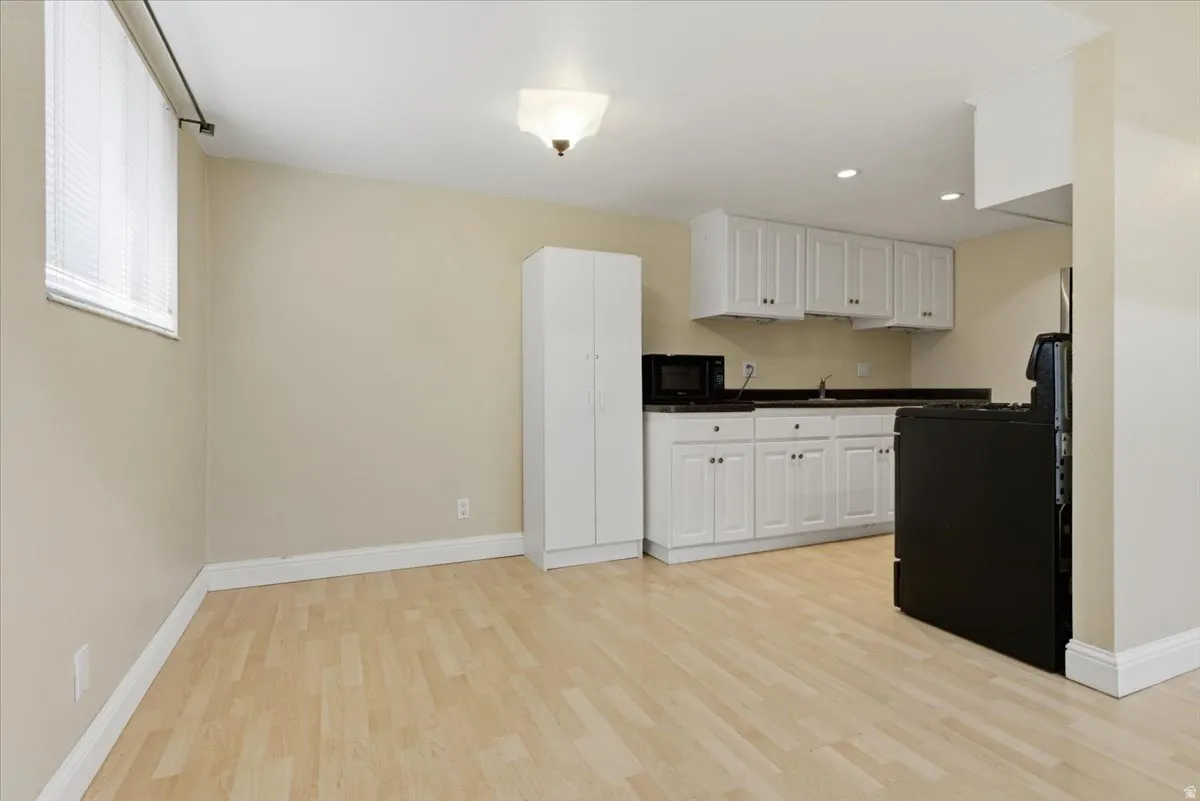 Kitchenette featuring white cabinetry, dark countertops, and a black range