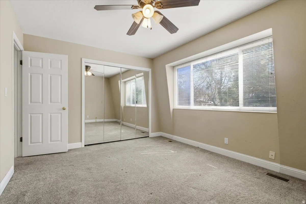Spacious room featuring neutral carpeting and a wide window with horizontal blinds