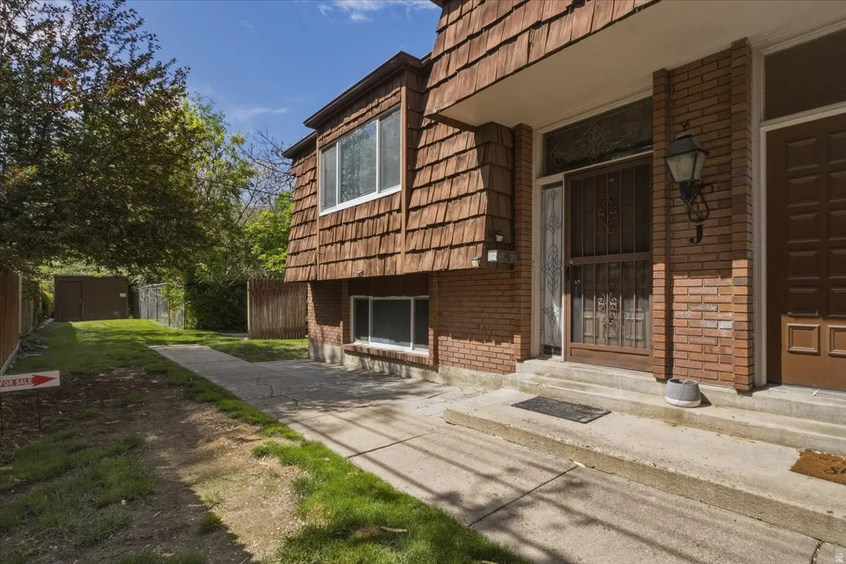 Brick and wood shake exterior featuring an ornate security screen door, a traditional outdoor lantern, and concrete steps