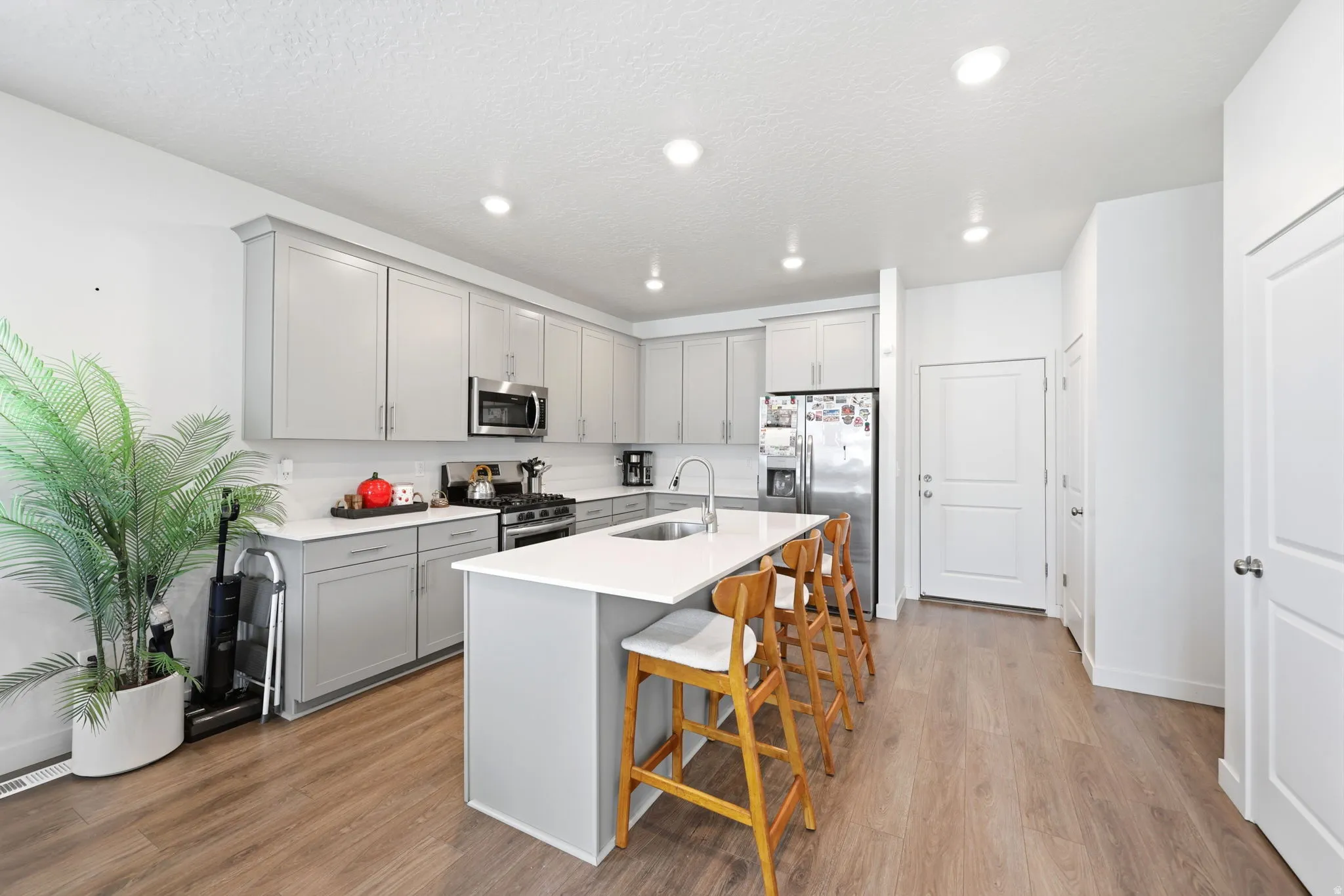 Kitchen featuring light gray cabinetry, stainless steel appliances, a center island with a sink, white countertops, and wood-finish flooring