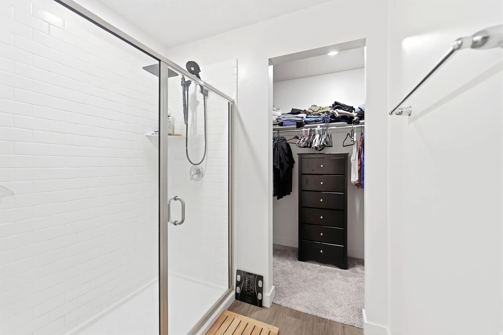 Walk-in shower with clear glass enclosure and subway tile surround, complemented by a recessed closet featuring carpeted flooring and recessed lighting