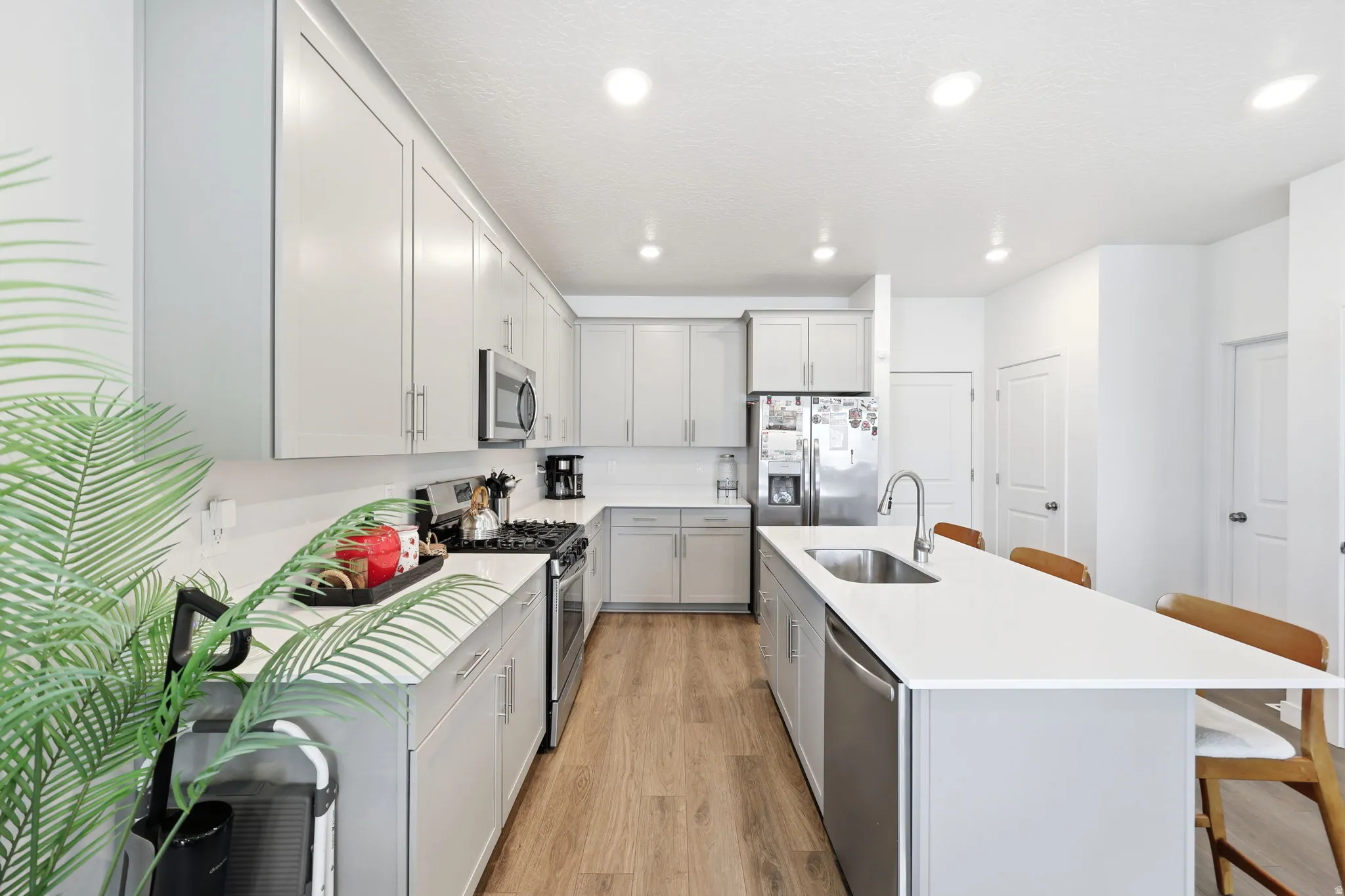 Modern kitchen featuring light gray cabinetry, stainless steel appliances, wood-finish flooring, recessed lighting, and a kitchen island with seating