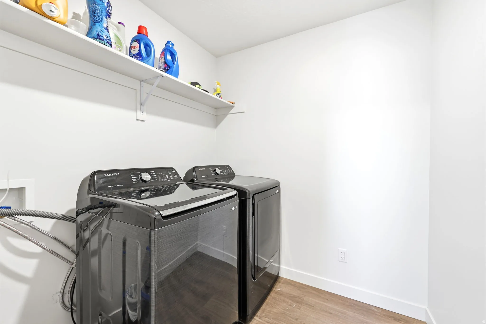 Dedicated laundry area featuring a washer and dryer, wood-finish flooring, and a white storage shelf