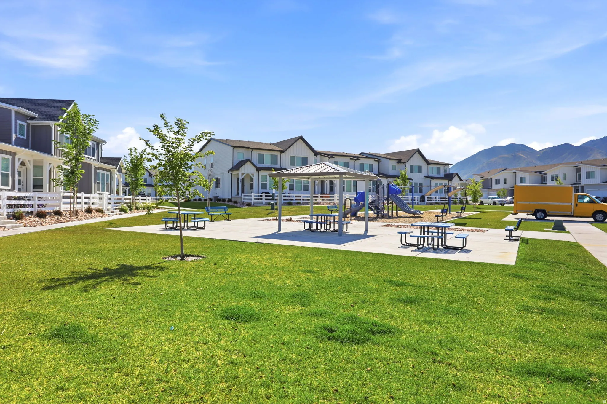 Community green space featuring a playground with slides and swings, covered picnic areas with benches, and extensive manicured lawns
