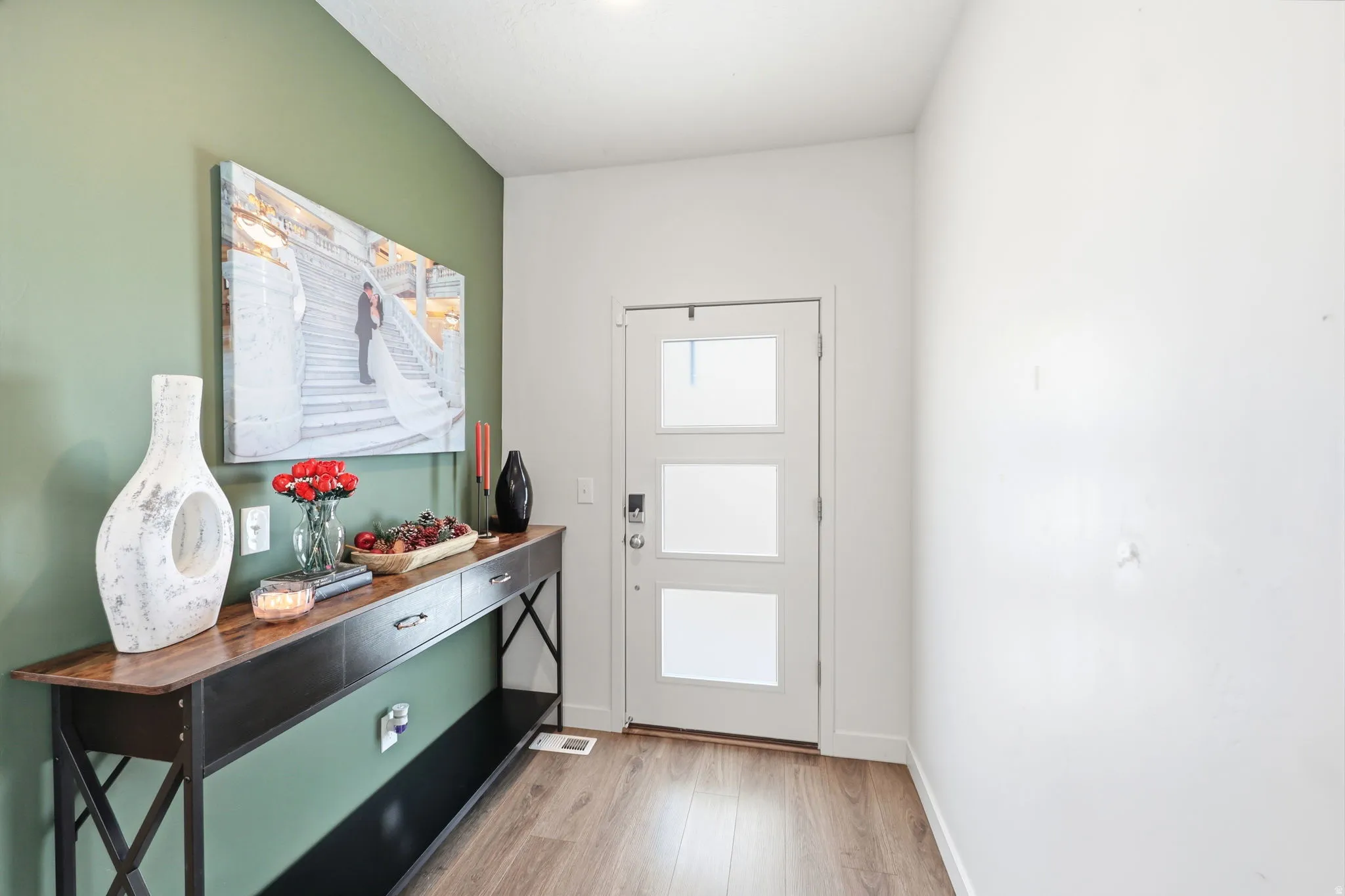 Entryway featuring a white door with three frosted glass panels, wood-finish flooring, and a green accent wall