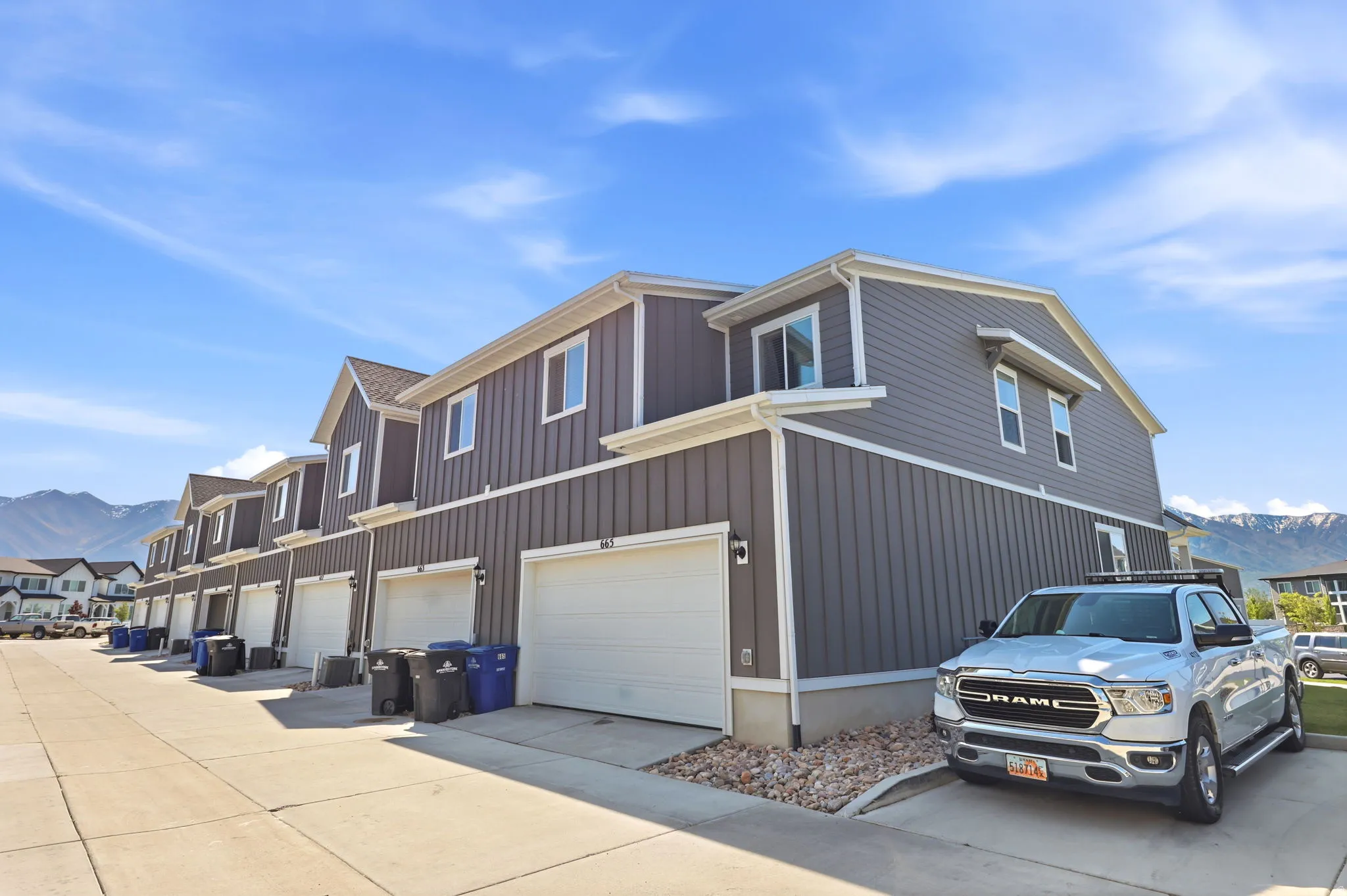 Contemporary townhome exterior with vertical siding, white trim accents, individual garage doors, and a concrete driveway