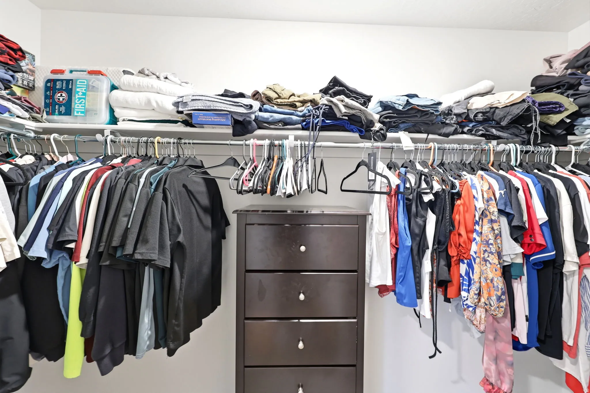 Walk-in closet featuring white walls, a dark wood-finish dresser with five drawers, and multiple clothing rods for ample storage