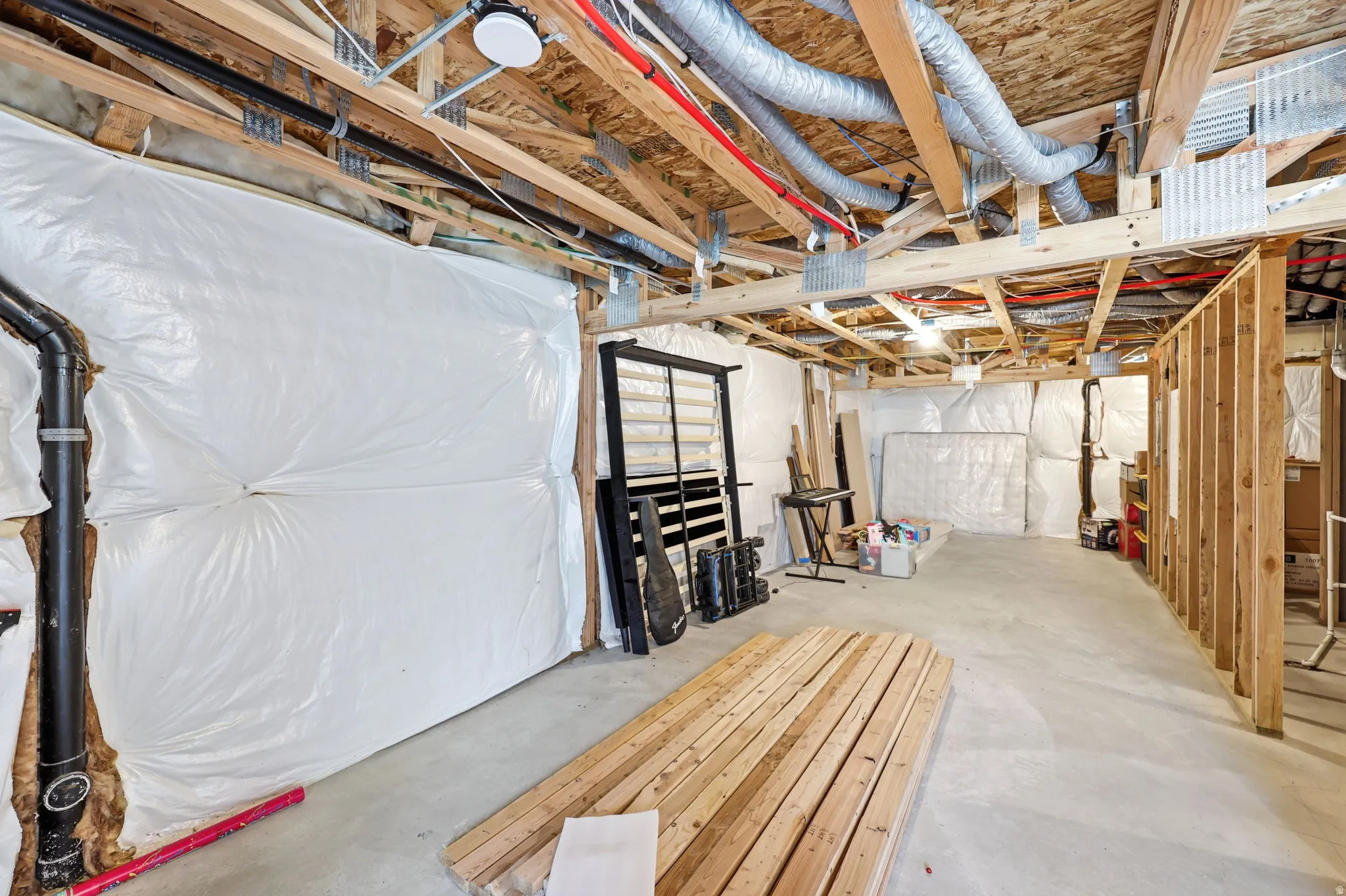 Unfinished basement with exposed wood framing, white insulation panels, concrete flooring, and visible ductwork and piping