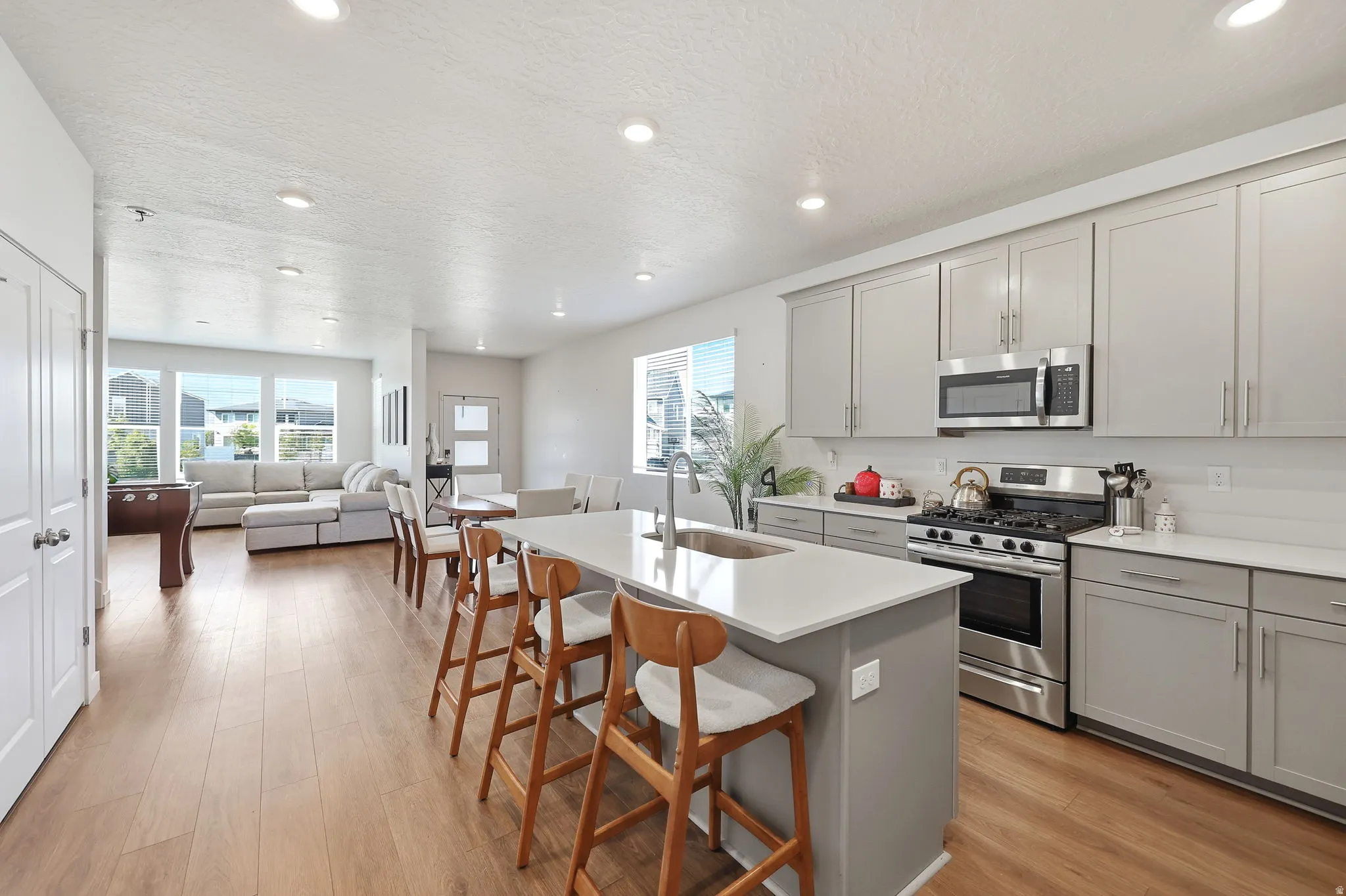 Contemporary kitchen featuring gray cabinetry, stainless steel appliances, and a central island with a sink and seating