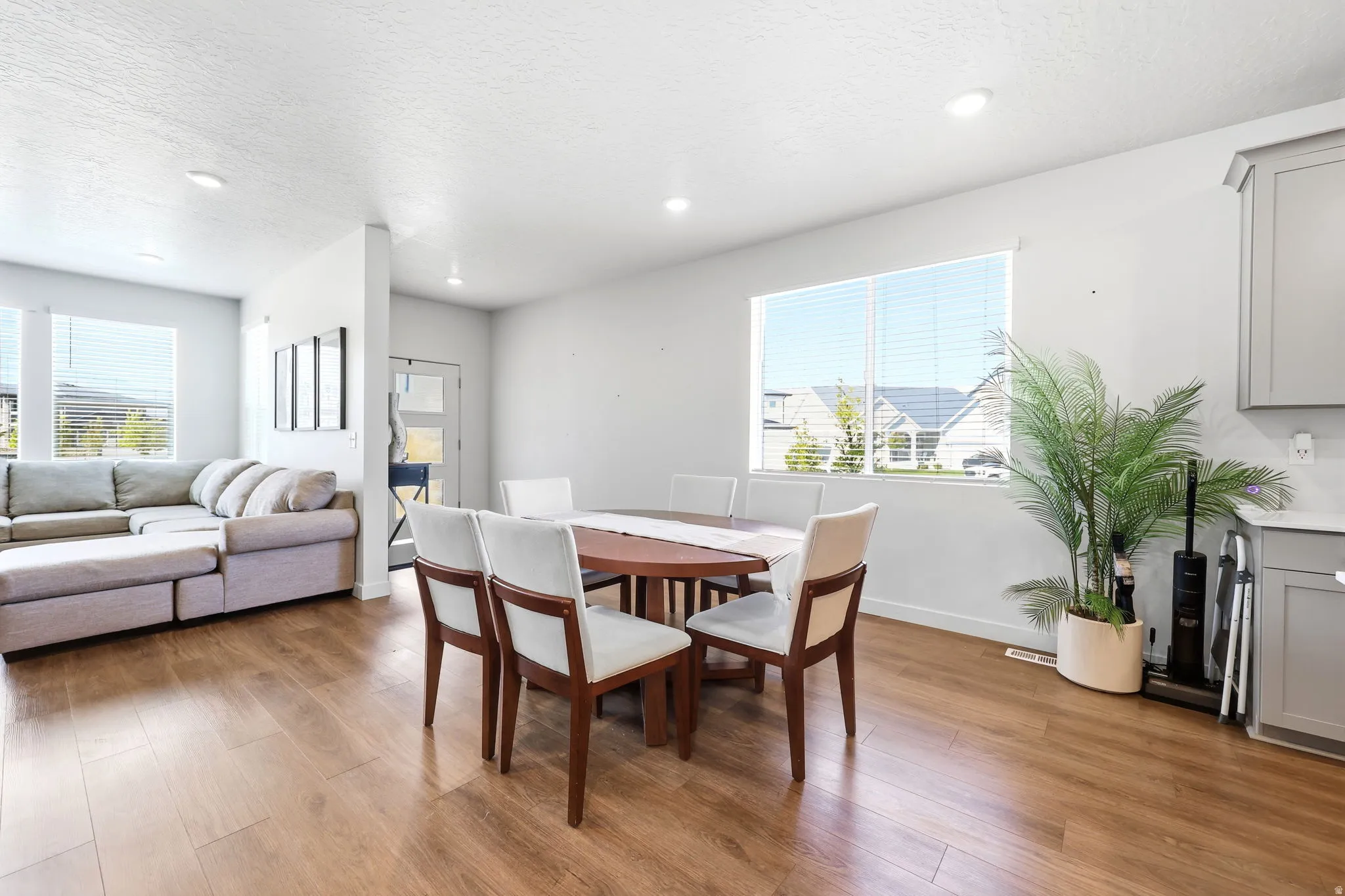 Open concept living area featuring wood-finish flooring, recessed lighting, and large windows with blinds