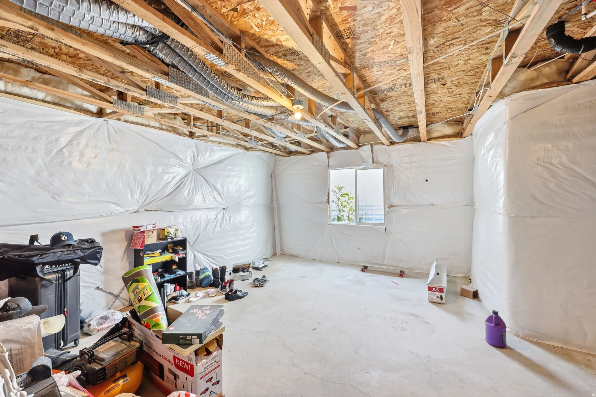 Unfinished basement space featuring exposed wood joists, ductwork, a concrete floor, and a vinyl-framed window