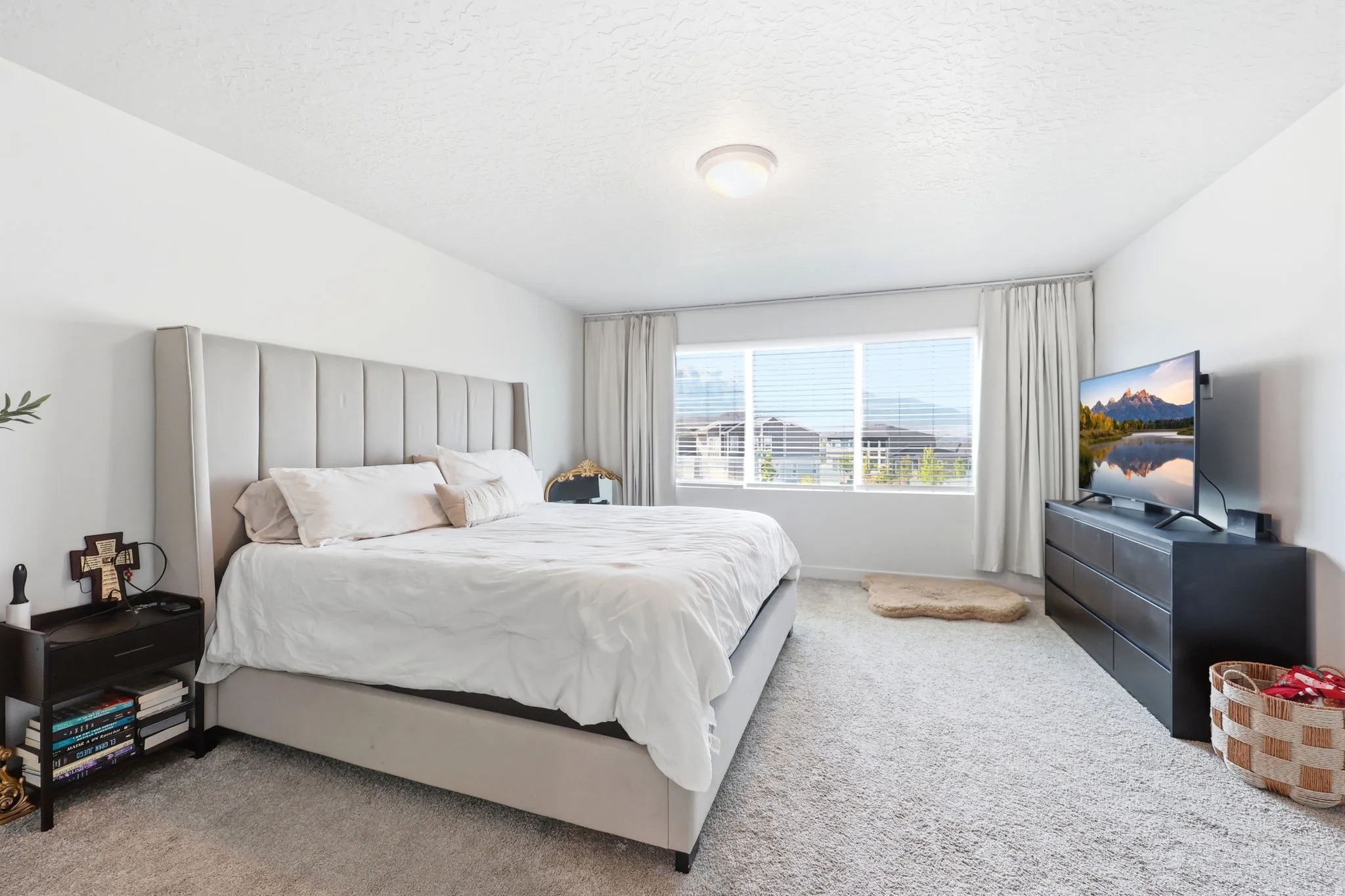 Bright room featuring neutral-toned walls, light-colored carpeting, a large window with blinds and drapes, and a flush-mount ceiling light fixture