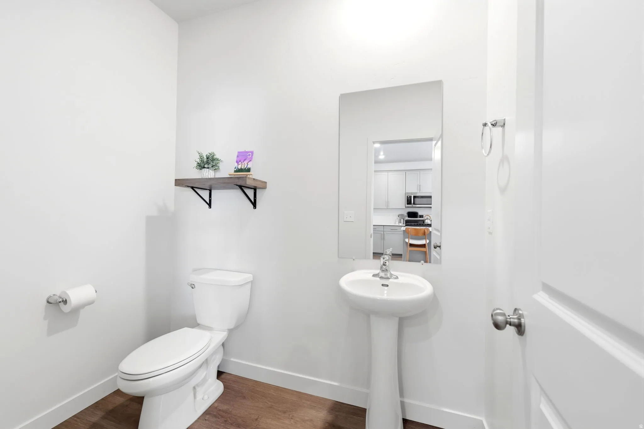 Powder room featuring a pedestal sink, wall-mounted mirror, and wood-finish flooring