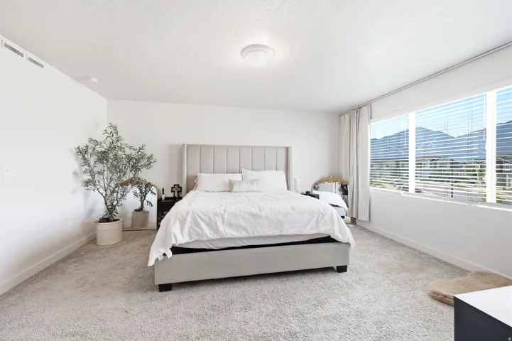 Bedroom featuring expansive windows with mountain scenery, light-colored carpet flooring, a contemporary ceiling light fixture, and white walls