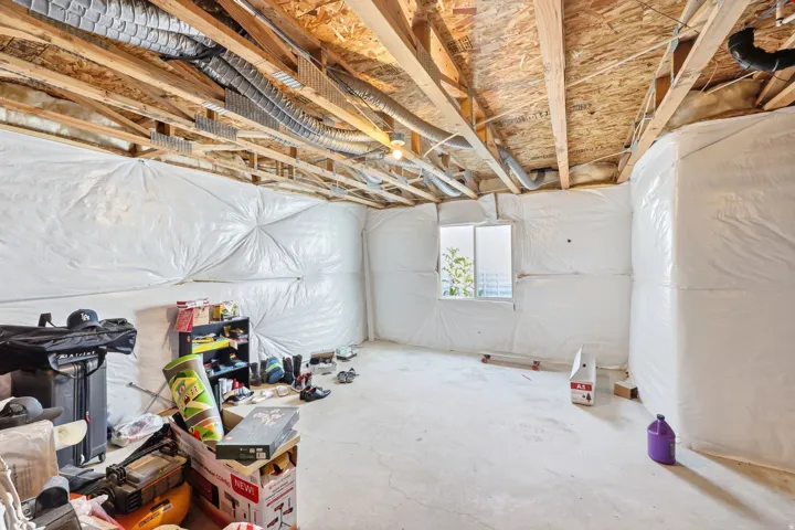 Unfinished basement space featuring exposed wood joists, ductwork, a concrete floor, and a vinyl-framed window