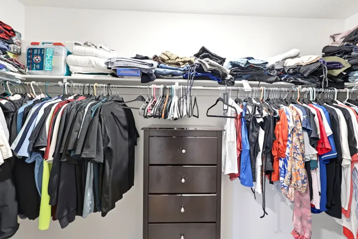 Walk-in closet featuring white walls, a dark wood-finish dresser with five drawers, and multiple clothing rods for ample storage