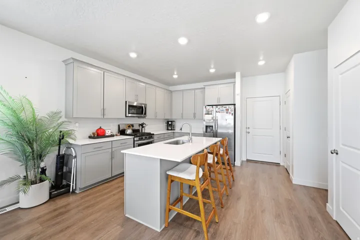 Kitchen featuring light gray cabinetry, stainless steel appliances, a center island with a sink, white countertops, and wood-finish flooring