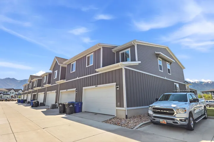 Contemporary townhome exterior with vertical siding, white trim accents, individual garage doors, and a concrete driveway