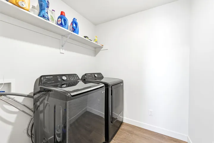 Dedicated laundry area featuring a washer and dryer, wood-finish flooring, and a white storage shelf