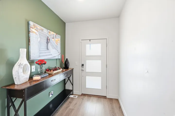 Entryway featuring a white door with three frosted glass panels, wood-finish flooring, and a green accent wall