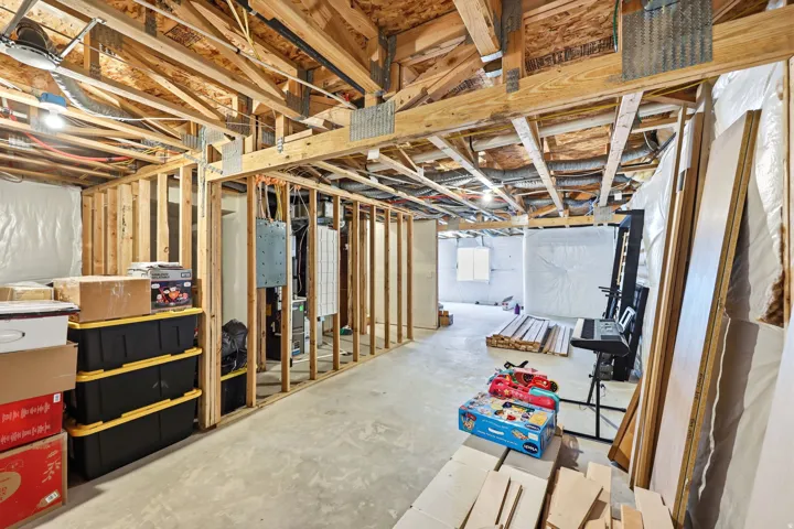 Unfinished basement featuring exposed wood framing, concrete flooring, and ample space for customization