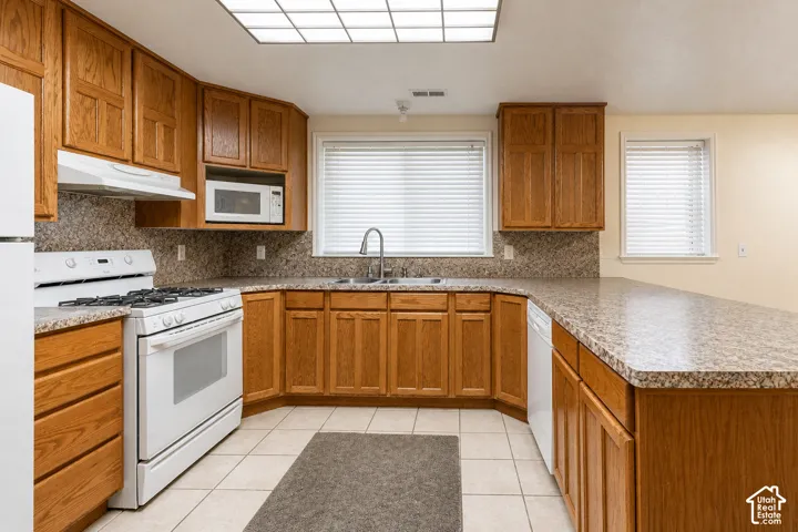 Well-appointed kitchen featuring wood cabinetry, white appliances, and a U-shaped countertop