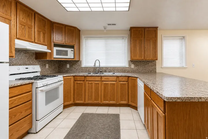 Well-appointed kitchen featuring wood cabinetry, white appliances, and a U-shaped countertop