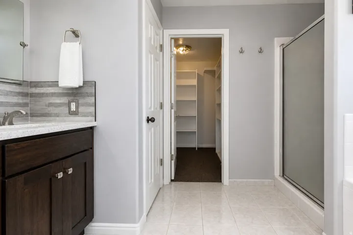 Primary Bathroom featuring a dark wood vanity with a light-toned countertop, a tiled backsplash, and a glass-enclosed shower