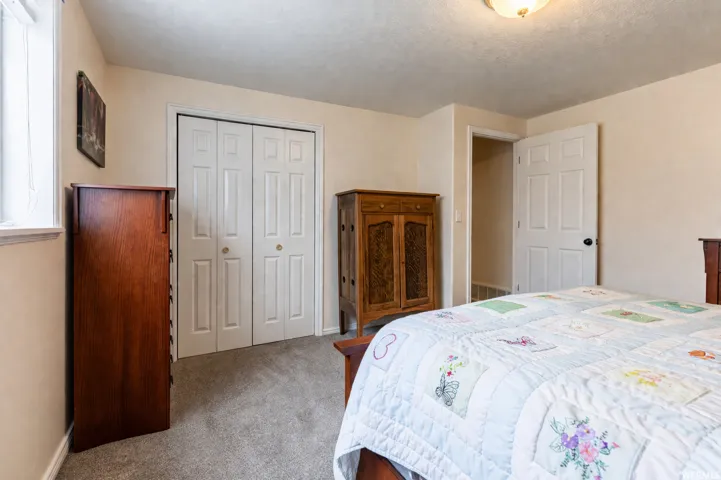 Bedroom featuring a window with white trim, a double bi-fold closet with panel doors, a five-panel interior door, carpet flooring, and a flush mount ceiling light fixture