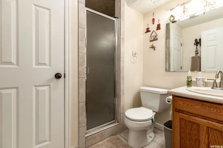 Bathroom featuring a glass-enclosed shower, light-toned wall tile, a white toilet, and a wood-finish vanity with a built-in sink and light-toned countertop