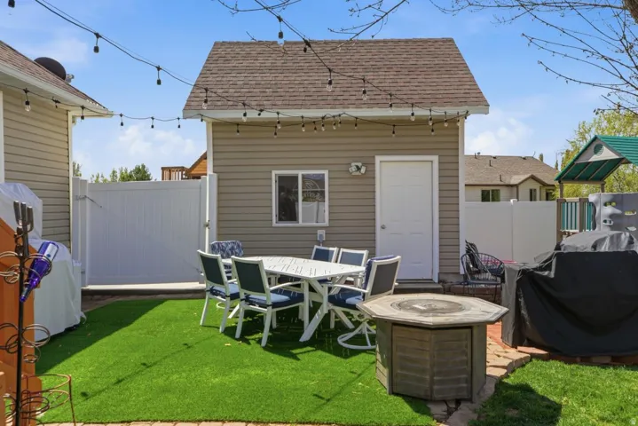 Private backyard featuring artificial turf, a brick patio, a detached structure with siding, and a white privacy fence
