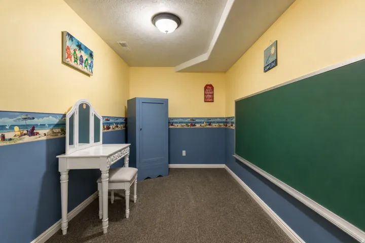 Carpeted room featuring a ceiling light fixture, a large green chalkboard, and two-toned walls with a decorative border