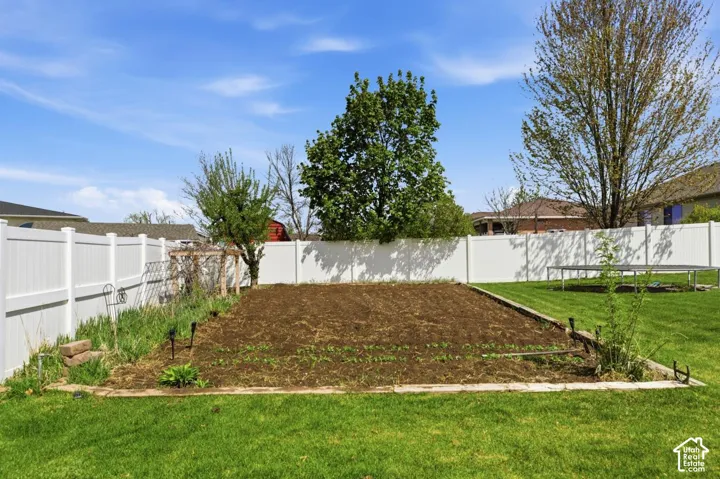 Expansive backyard featuring a large garden bed, lush green lawn, full privacy fencing, mature trees, and a wooden arbor