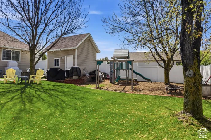 Expansive backyard featuring a manicured lawn, a detached accessory building with tan siding, a white privacy fence, and mature trees providing shade