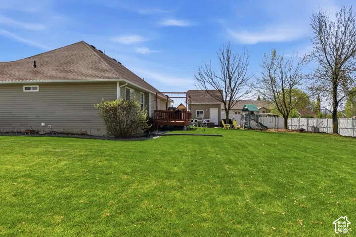 Expansive grassy yard with a wooden deck, a detached shed, and a white privacy fence