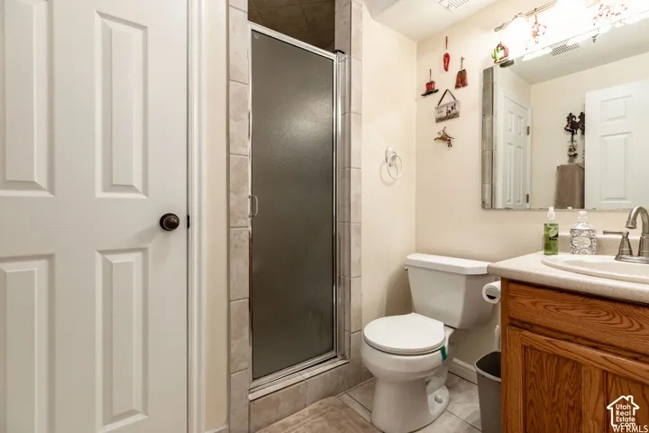 Bathroom featuring a glass-enclosed shower, light-toned wall tile, a white toilet, and a wood-finish vanity with a built-in sink and light-toned countertop