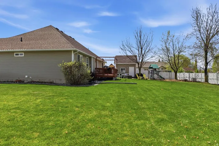 Expansive grassy yard with a wooden deck, a detached shed, and a white privacy fence