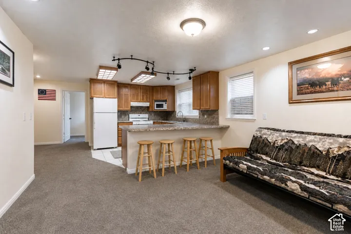 Open-concept living area featuring a kitchen with wood cabinetry, a breakfast bar with stone-finish countertop, and full-size appliances